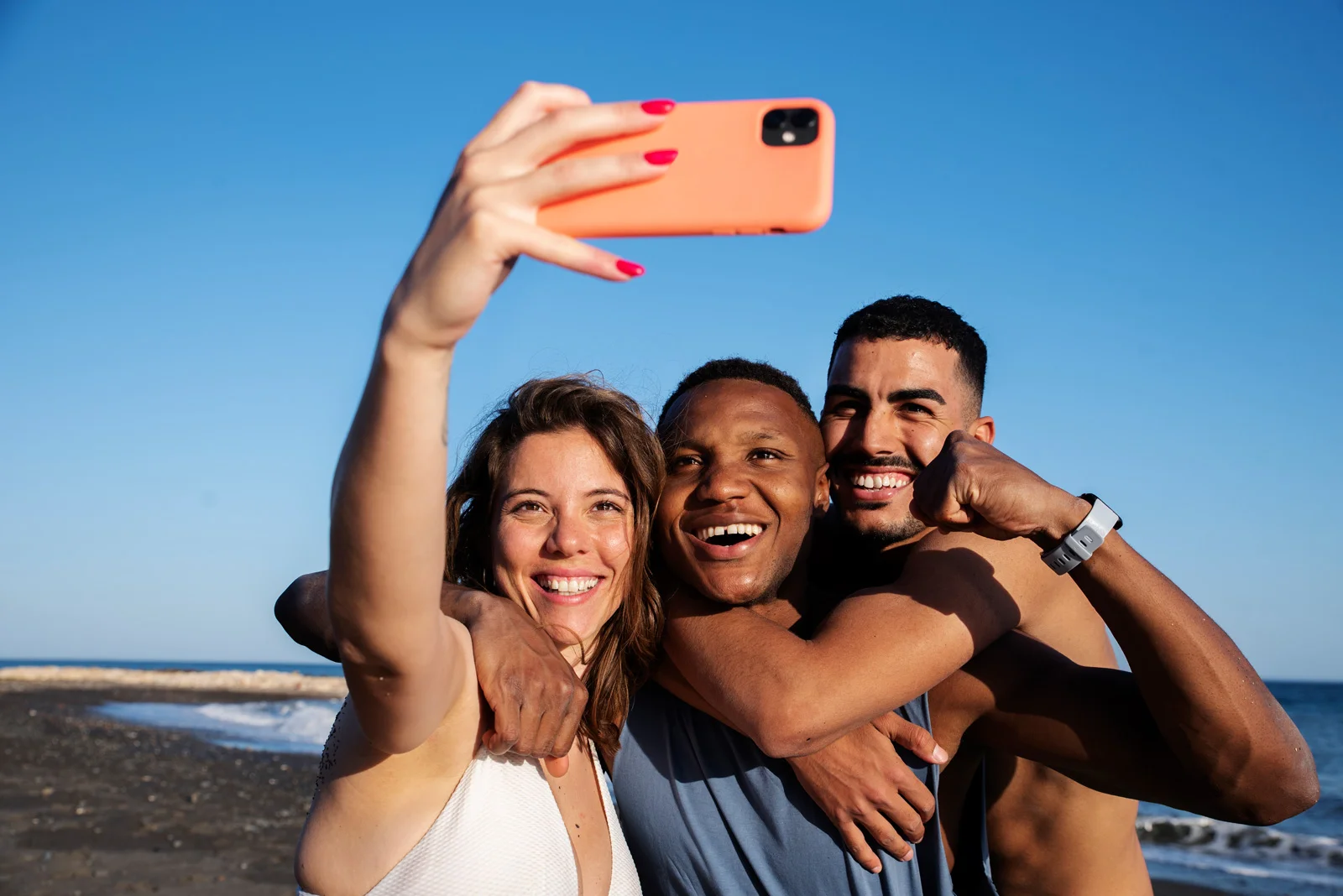 Drei junge Personen machen ein Selfie am Strand